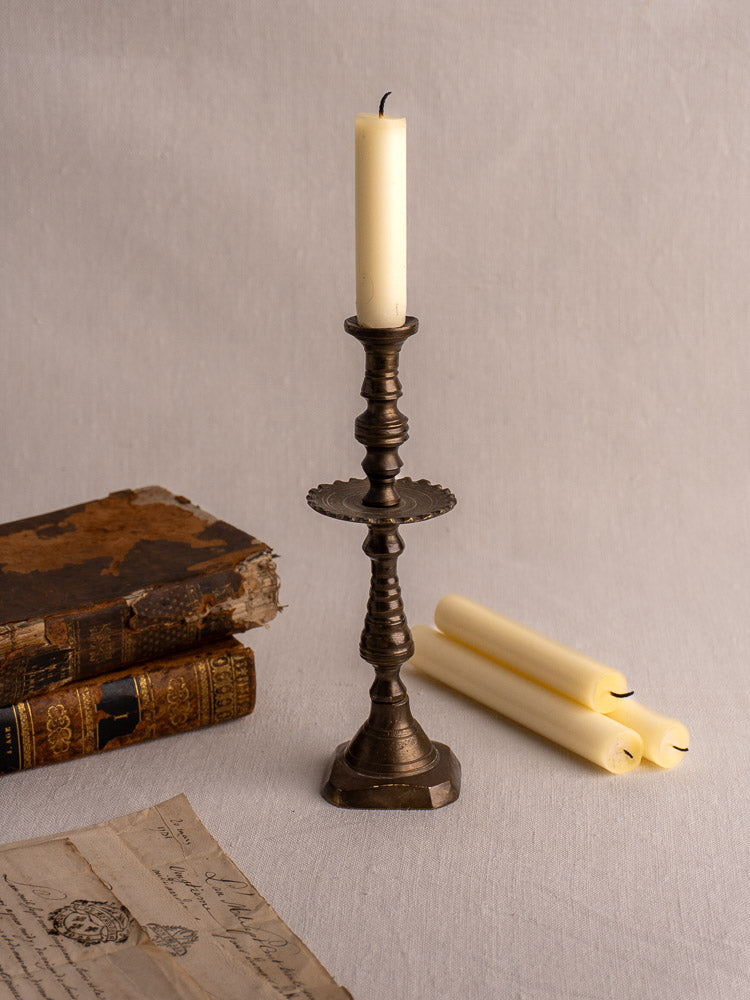 19th-century French brass candlestick with scalloped drip pan on textured light fabric backdrop.