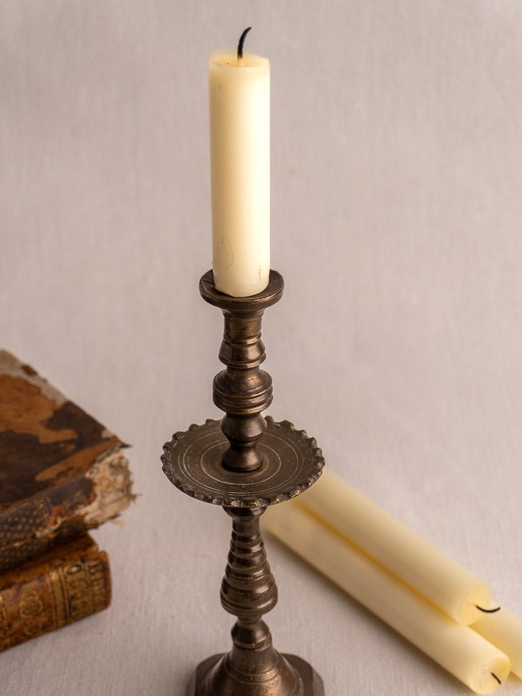 Antique French brass candlestick with unlit white candle, beside two rolled candles and vintage book.