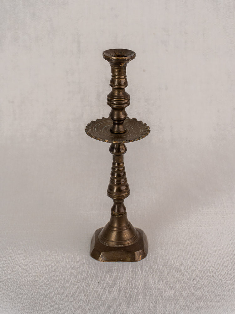 19th-century French brass candlestick with scalloped drip pan on textured light fabric backdrop.