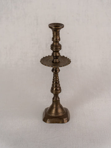 19th-century French brass candlestick with scalloped drip pan on textured light fabric backdrop.