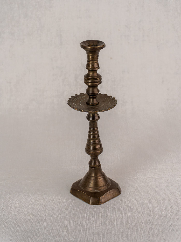 Antique 19th-century French brass candlestick with scalloped drip pan and hexagonal base on white background.