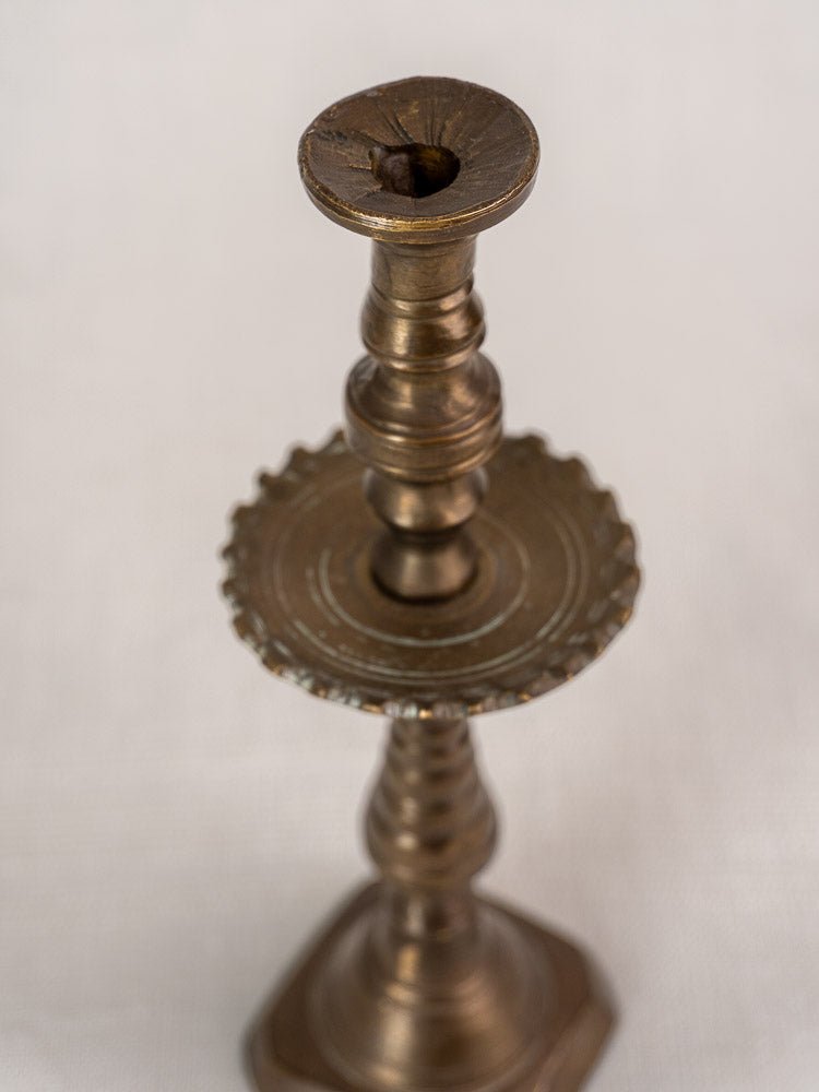Antique French brass candlestick with ornate details and scalloped drip pan on a light background.