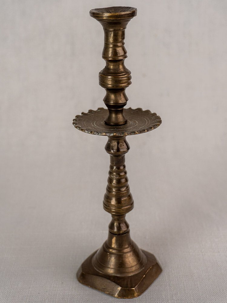 Antique French brass candlestick with ornate detailing and scalloped mid-shaft drip pan on square base.