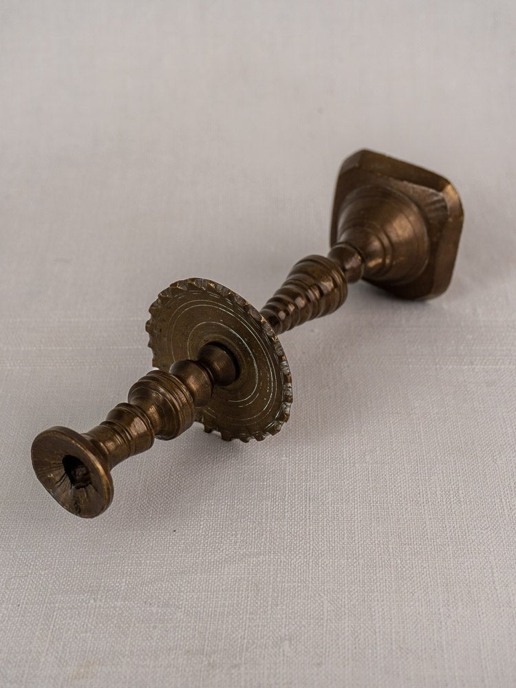 Antique French brass candlestick with scalloped drip pan and intricate engravings on light fabric surface.