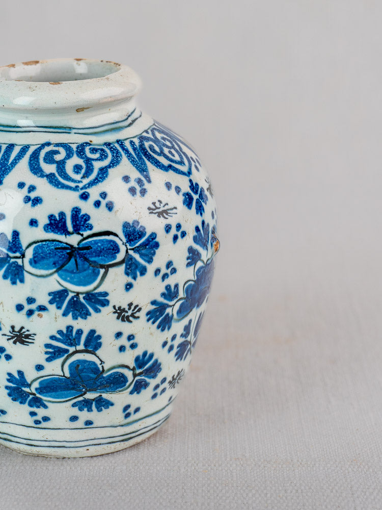 Antique Dutch Delft blue and white faience vase with intricate chinoiserie patterns and softly worn rim against a pale background.