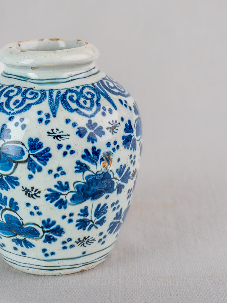 Antique Dutch Delft blue and white faience vase with chinoiserie floral motifs and a slightly chipped top rim.