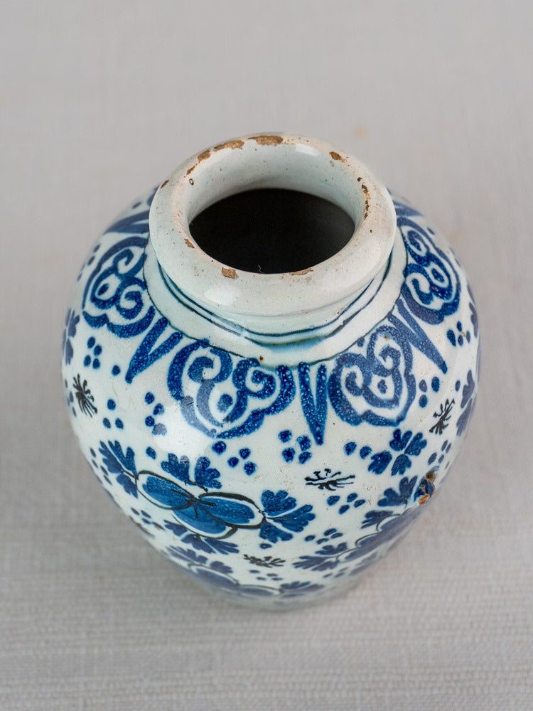 18th-century Dutch Delft faience vase with blue floral patterns, wide opening, worn rim, shown on a textured surface.