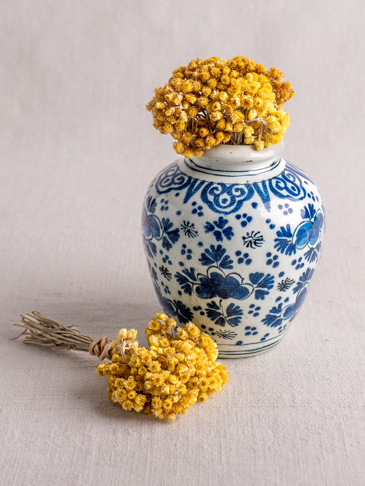 Antique 18th-century Dutch Delft blue and white faience vase with yellow dried flowers on a light beige surface.