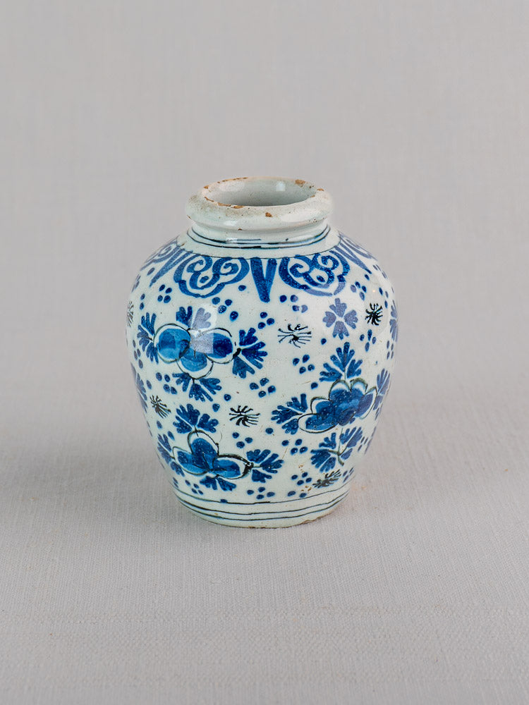 Antique Dutch Delft blue and white faience vase with floral chinoiserie design and narrow neck on light gray surface.