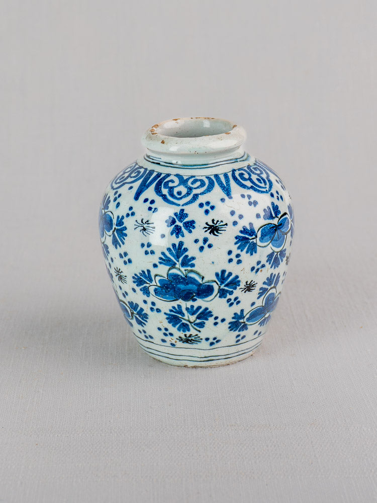 Antique 18th century Dutch Delft vase in blue and white faience with chinoiserie floral and geometric motifs on light gray surface.