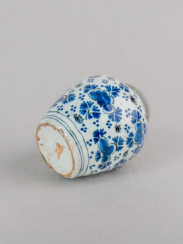 18th century Dutch Delft blue and white faience vase with chinoiserie floral motifs, base wear, unglazed ring on gray surface.