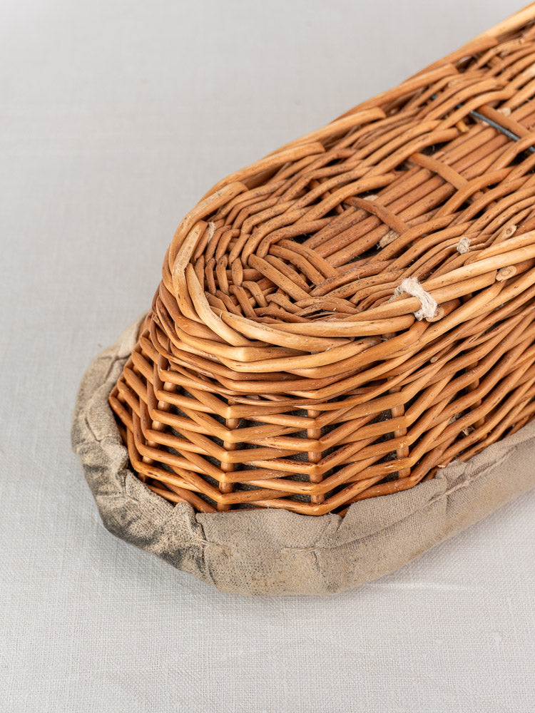Vintage French baguette proofing baskets with linen liners, intricate weaving and solid craftsmanship on a light background.