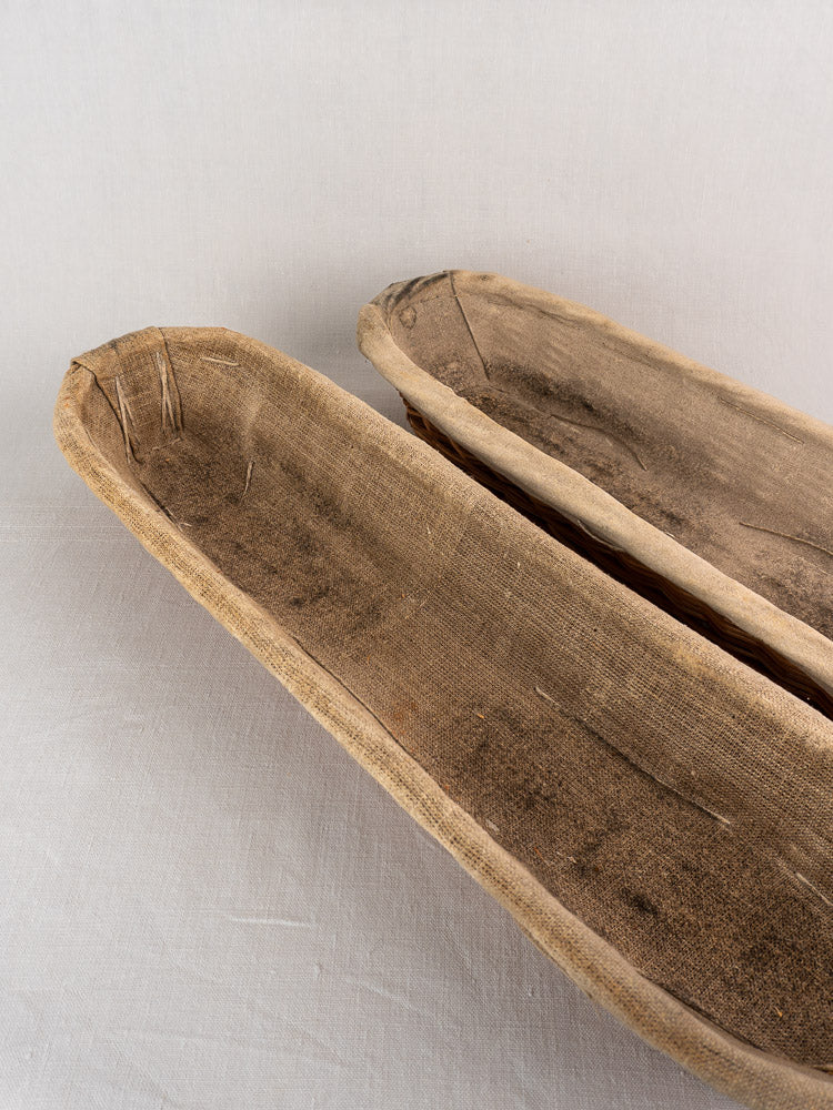 Pair of vintage French baguette proofing baskets from 1940-1950, linen-lined, on light fabric surface.