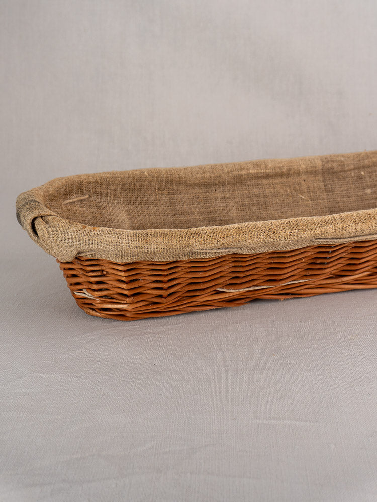 Vintage French baguette proofing basket from the 1940s-1950s with beige linen liner on light gray textured surface.