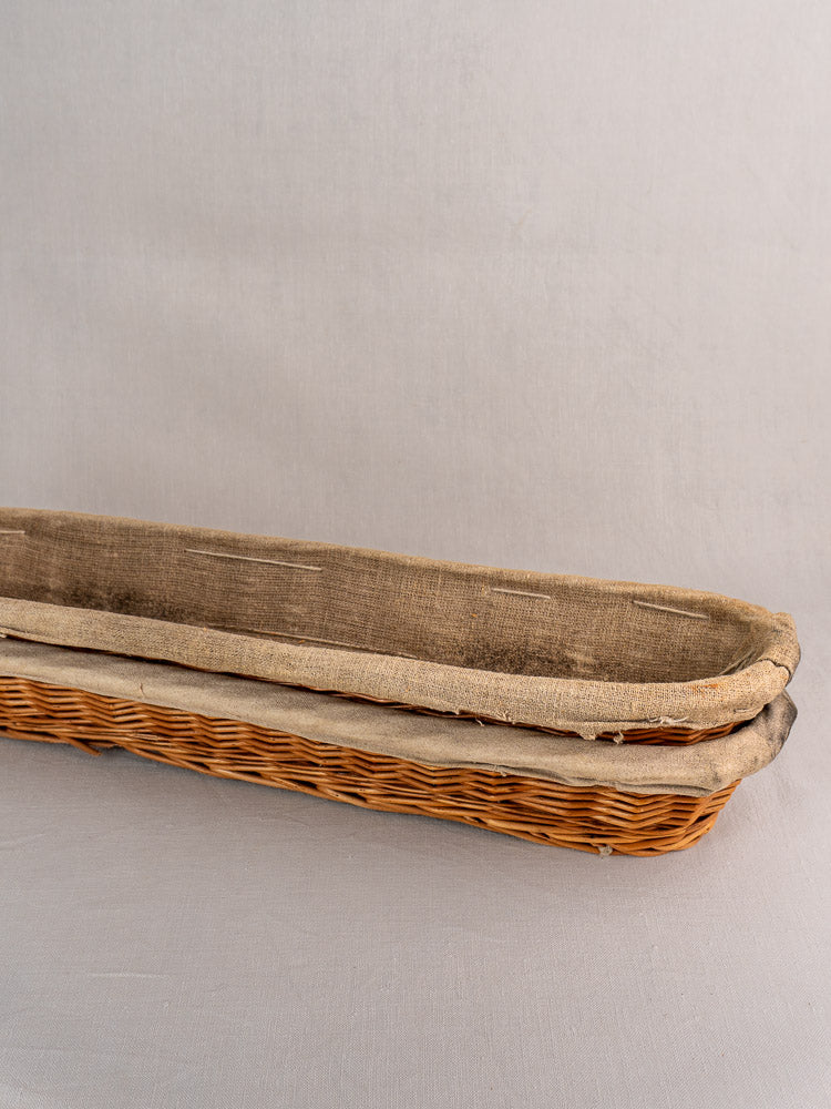 Vintage French baguette proofing basket with rustic beige linen liner, 1940s–1950s, on light gray surface.