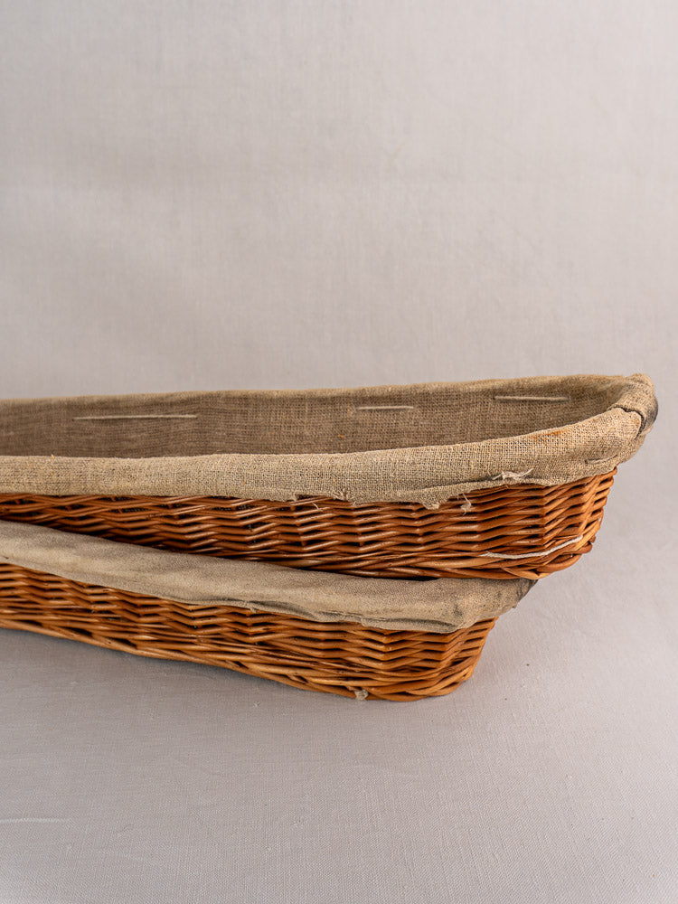 Pair of vintage French baguette proofing baskets with linen liners, stacked on a neutral surface.