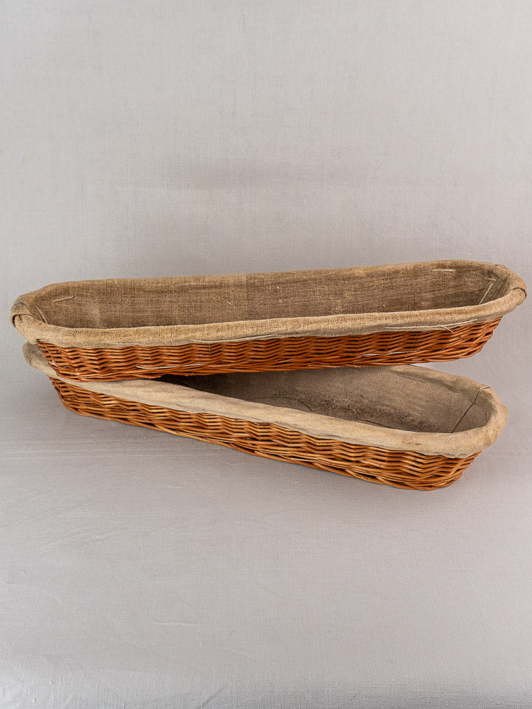 Pair of vintage French baguette proofing baskets, circa 1940-1950, linen-lined, stacked on light gray surface.