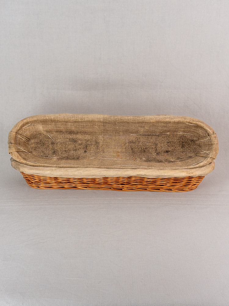 Vintage French baguette proofing basket from 1940-1950 with linen lining on a light gray surface.