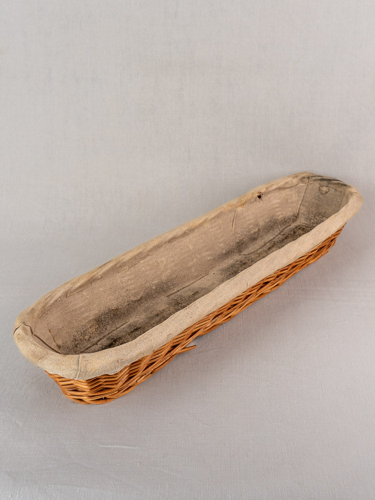 Vintage French baguette proofing basket with linen liner from 1940-1950s, showing gentle wear on a light gray surface.