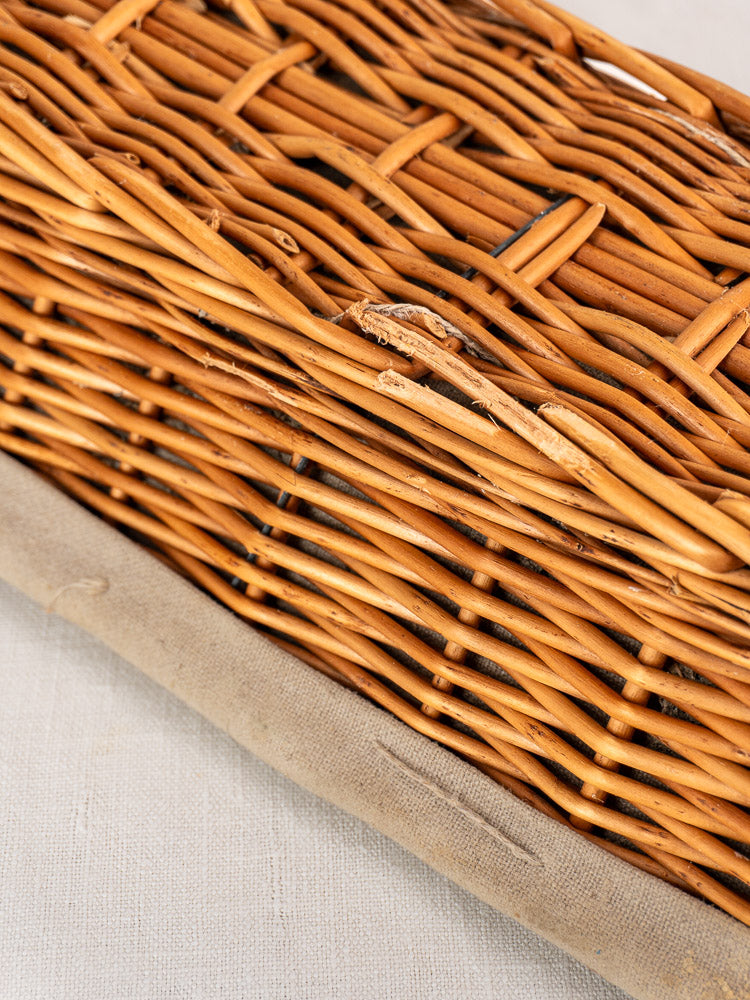 Vintage French baguette proofing baskets with linen liners, minor wicker wear, on light beige fabric surface.
