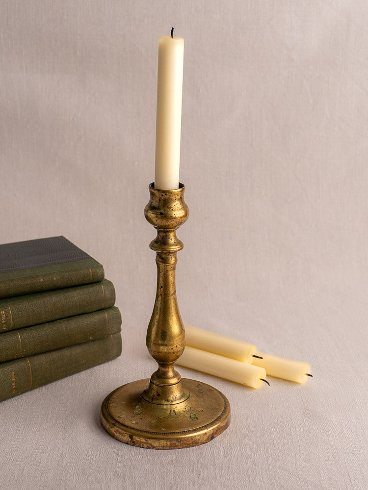 Antique French brass candlestick, 19th century, with turned baluster stem and round base on neutral background.