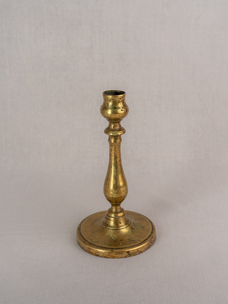 Antique French brass candlestick, 19th century, with turned baluster stem and round base on neutral background.