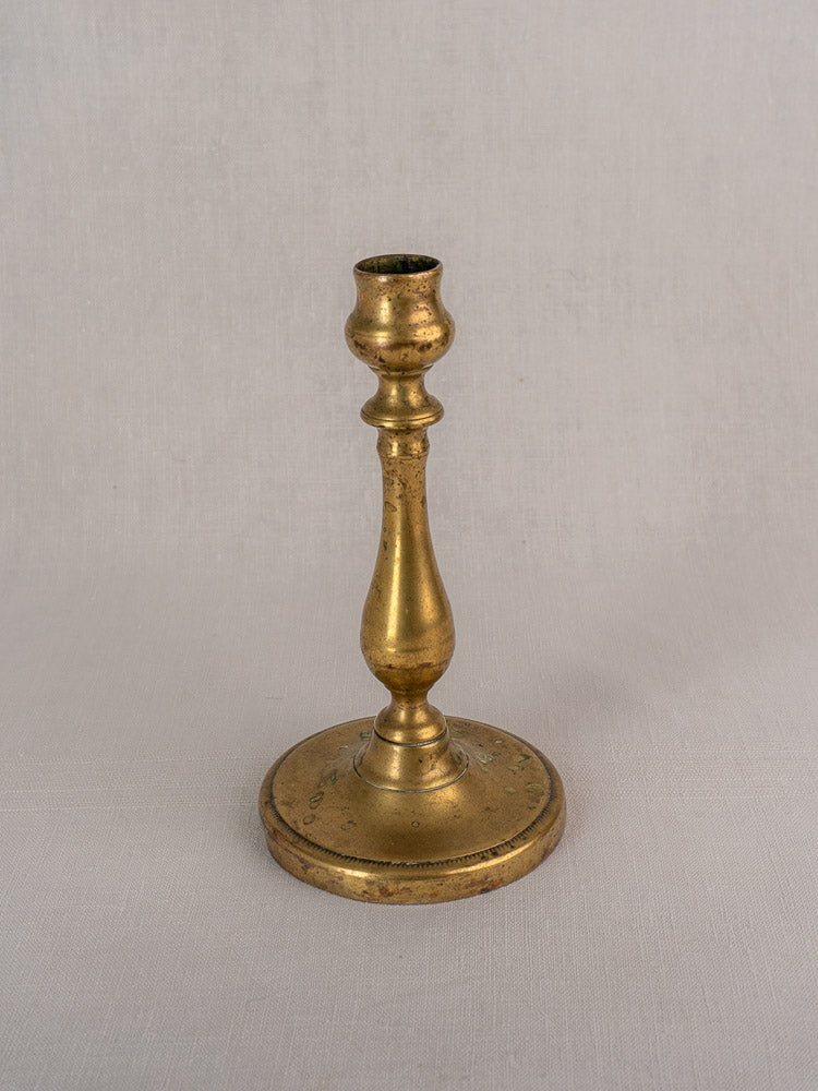 Antique French brass candlestick with turned baluster stem and round base on light gray surface.