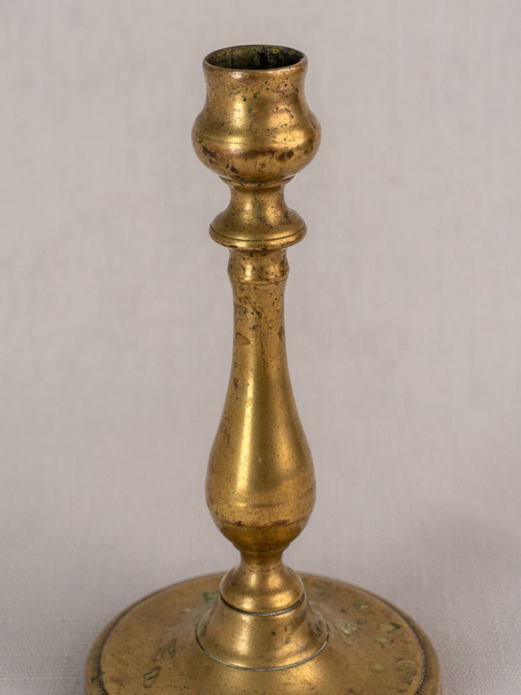 Antique French brass candlestick, 19th century, with turned baluster stem and rounded base on plain background.