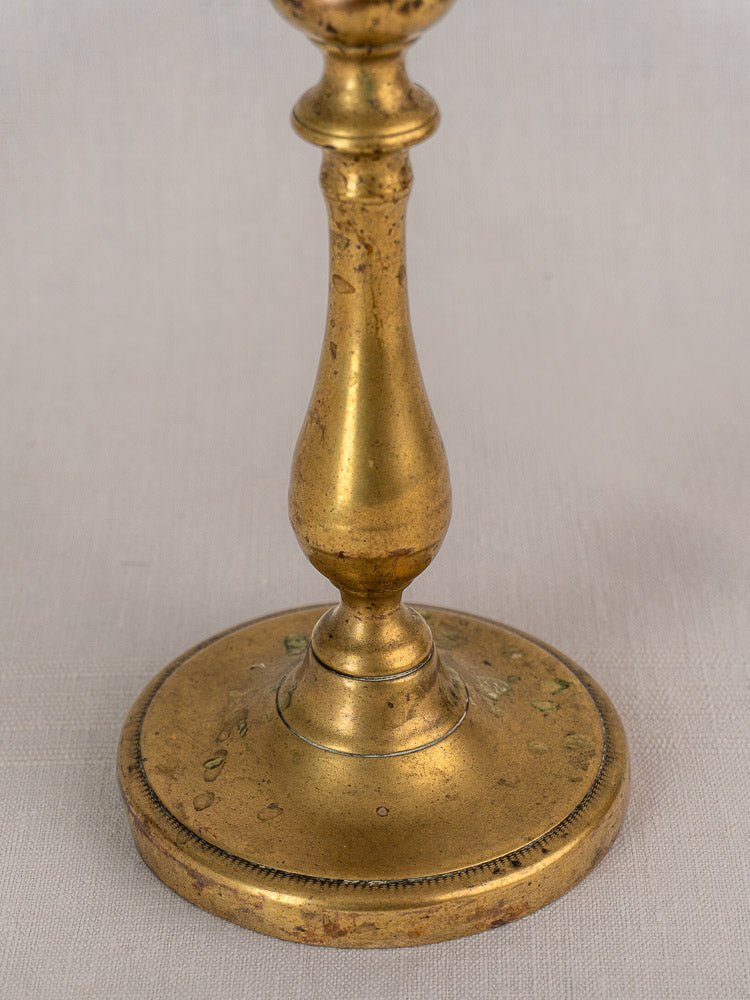 Antique French brass candlestick with a turned baluster stem on a light textured surface.