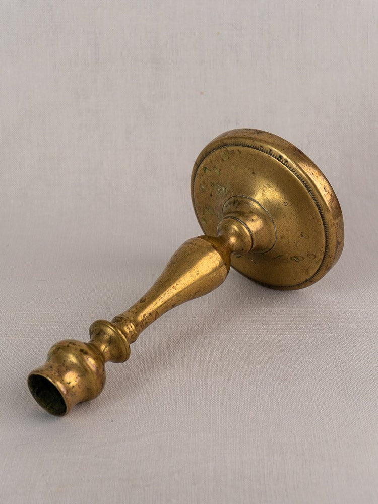 Antique French brass candlestick with baluster stem, 19th century, on light gray fabric.