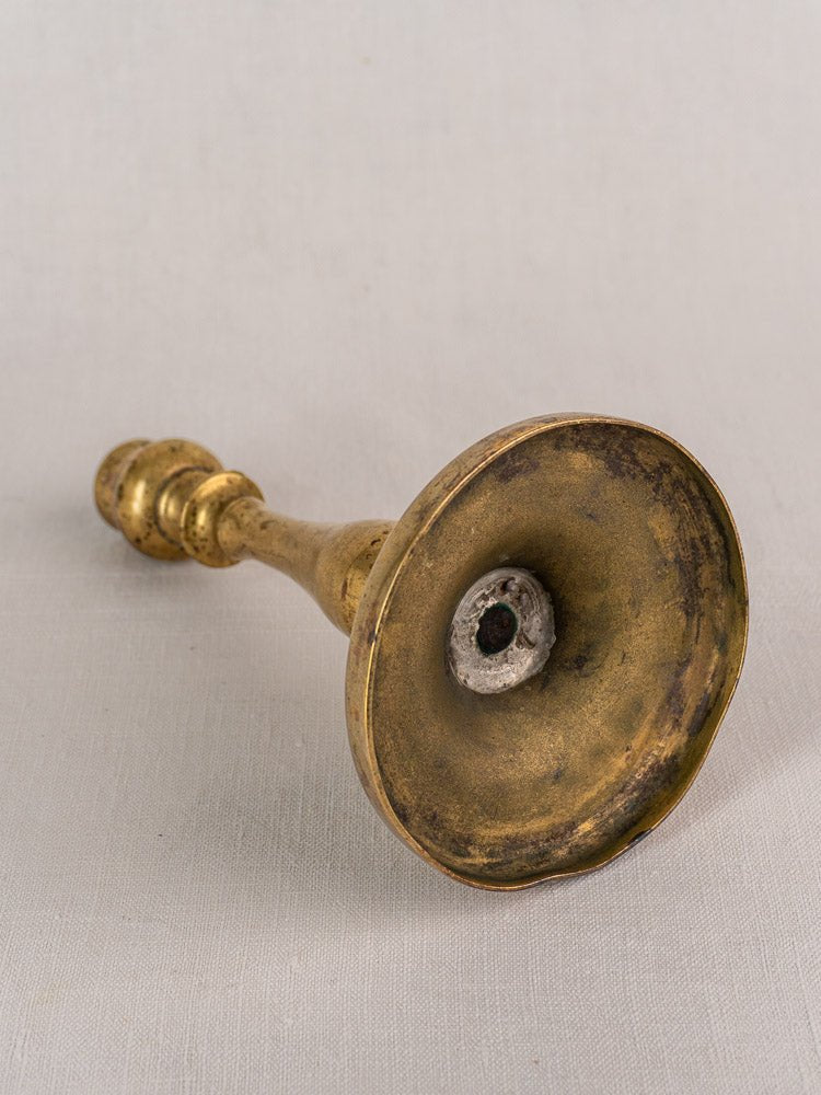 Antique French brass candlestick with baluster stem, wide base, on light textured surface.