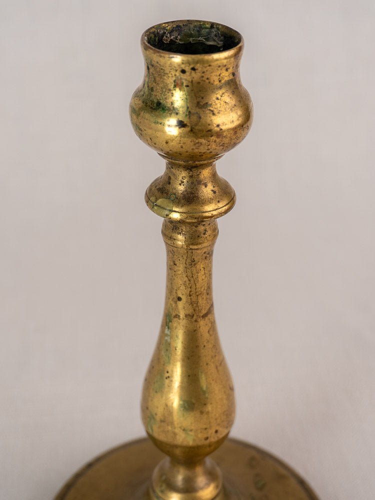 Antique French brass candlestick with turned baluster stem and rounded base, lightly tarnished, on light background.