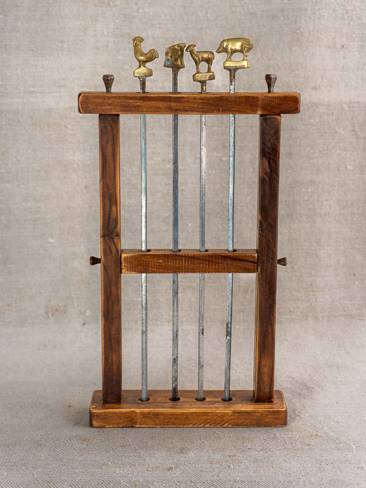 Vintage French brochette skewers set with brass animal finials and wooden stand on neutral fabric background.