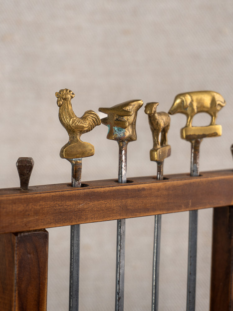 Set of four metal brochette skewers with brass animal finials in a wooden holder.