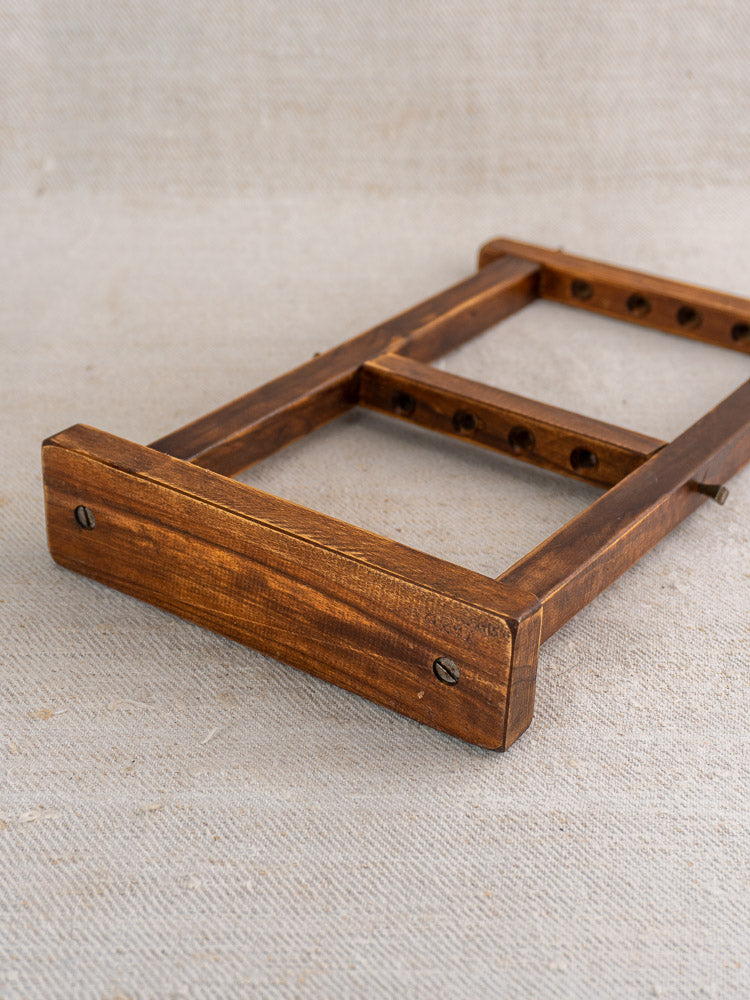 Compact wooden stand with evenly spaced holes and end blocks on a textured beige fabric background.
