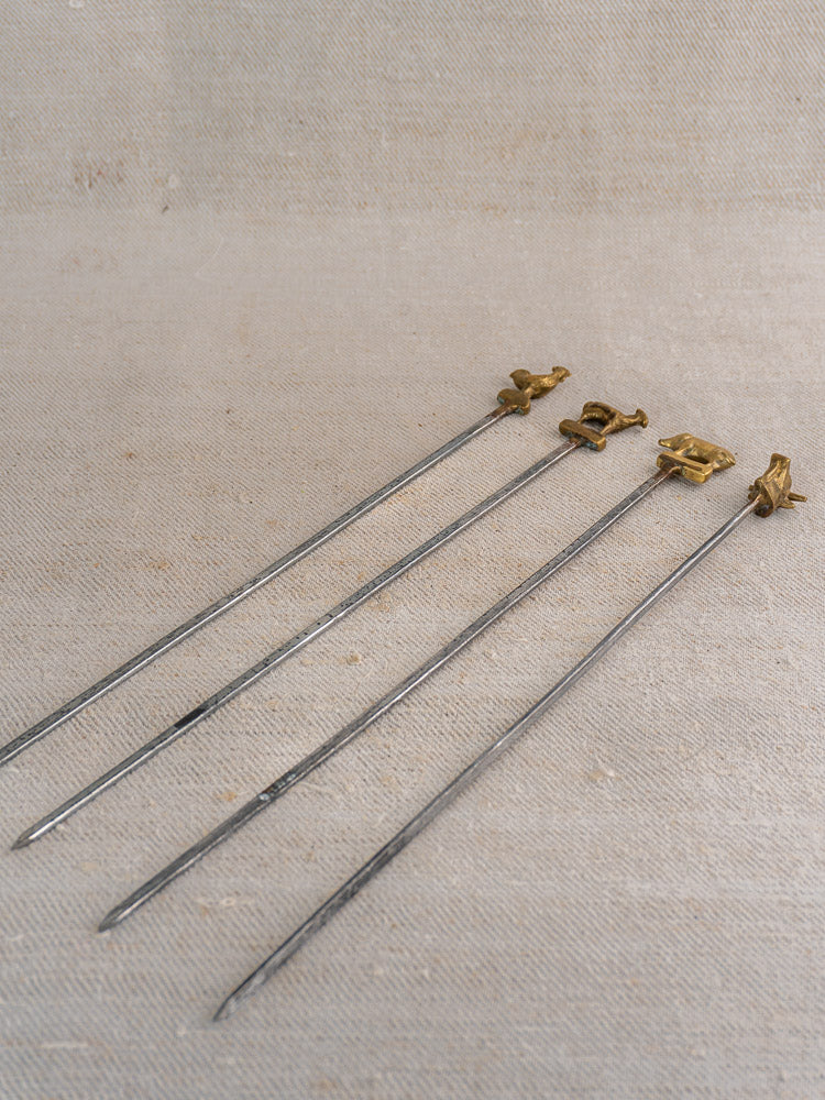 Vintage French brochette skewers with brass animal finials on beige fabric, includes wooden stand.