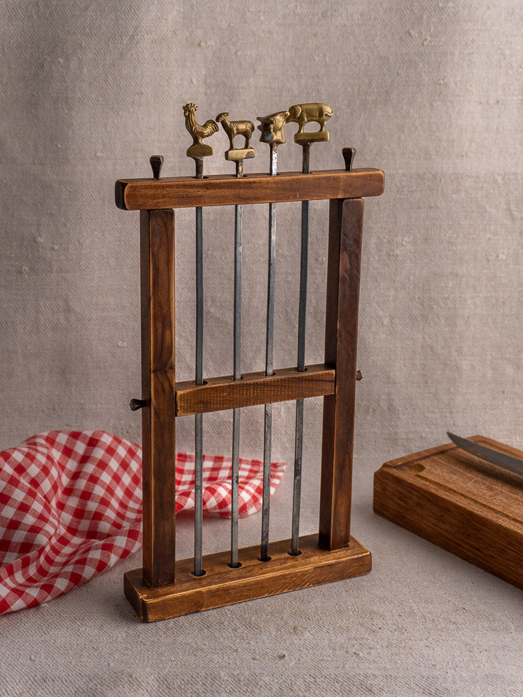 Vintage French brochette skewers set of five brass animal finials in wooden stand on beige fabric.