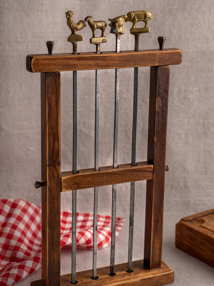 Vintage French brochette skewers with brass chicken, goat, and cow finials on wooden stand.