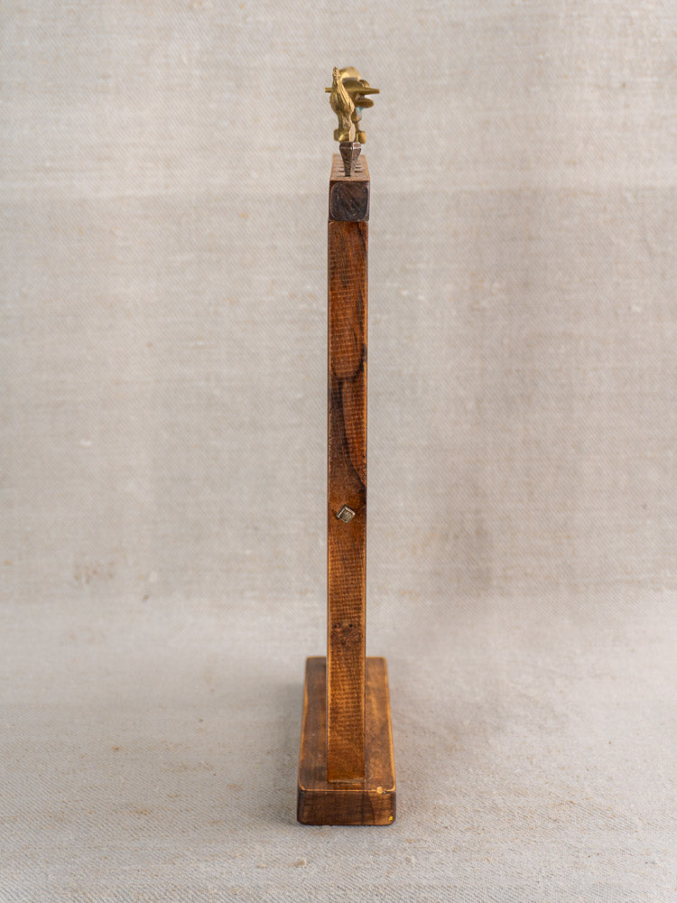 Vintage French wooden stand with upright brochette skewers, brass animal finials, on neutral fabric background.