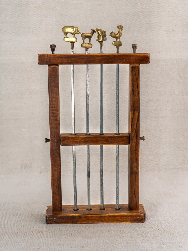 Vintage French brochette skewers set with brass animal finials in wooden stand on beige fabric.