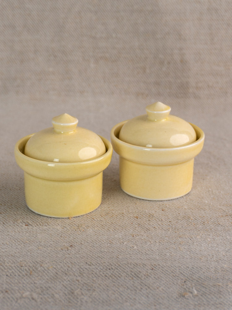 Pair of vintage French cream-glazed butter pots from the mid-20th century on neutral textured fabric.