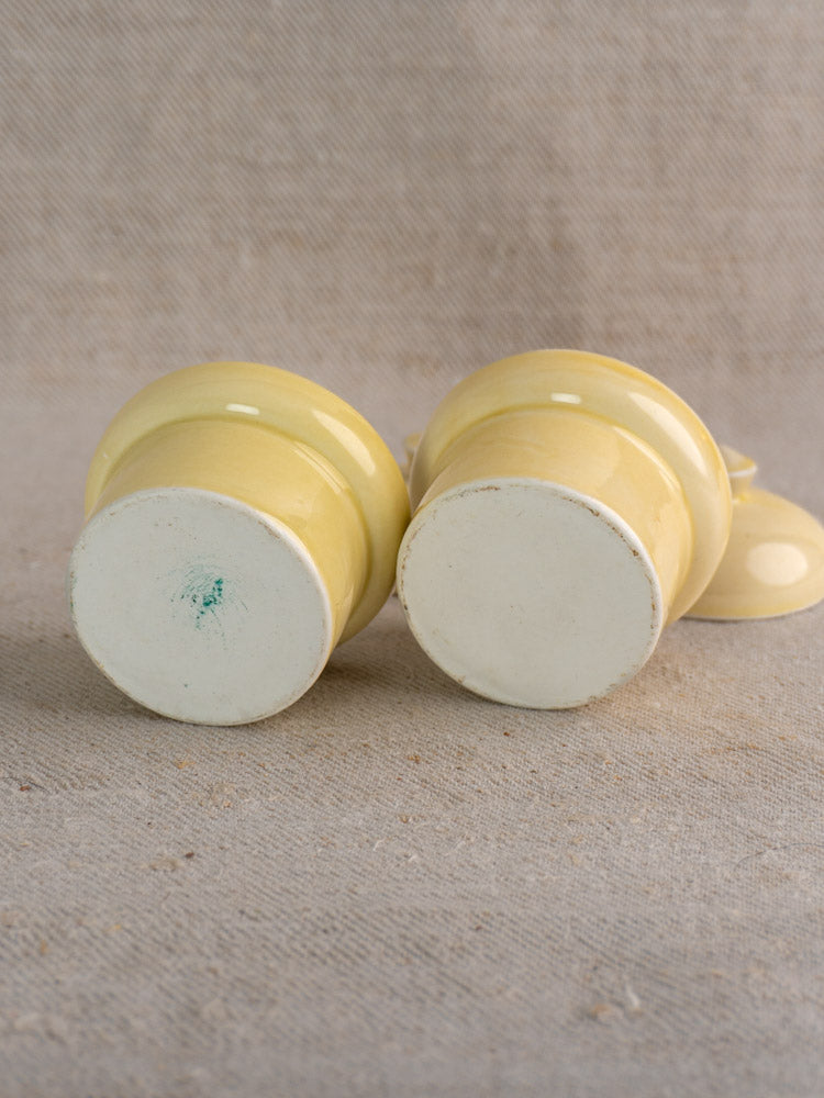 Pair of mid-20th century vintage French cream-glazed butter pots showing marked unglazed bases on neutral textured fabric.