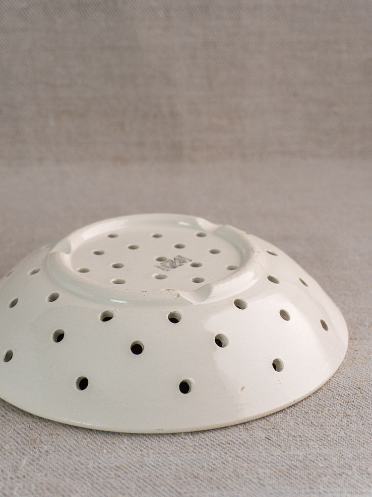 Antique French Digoin Sarreguemines stoneware berry strainer upside down on beige textured fabric background.