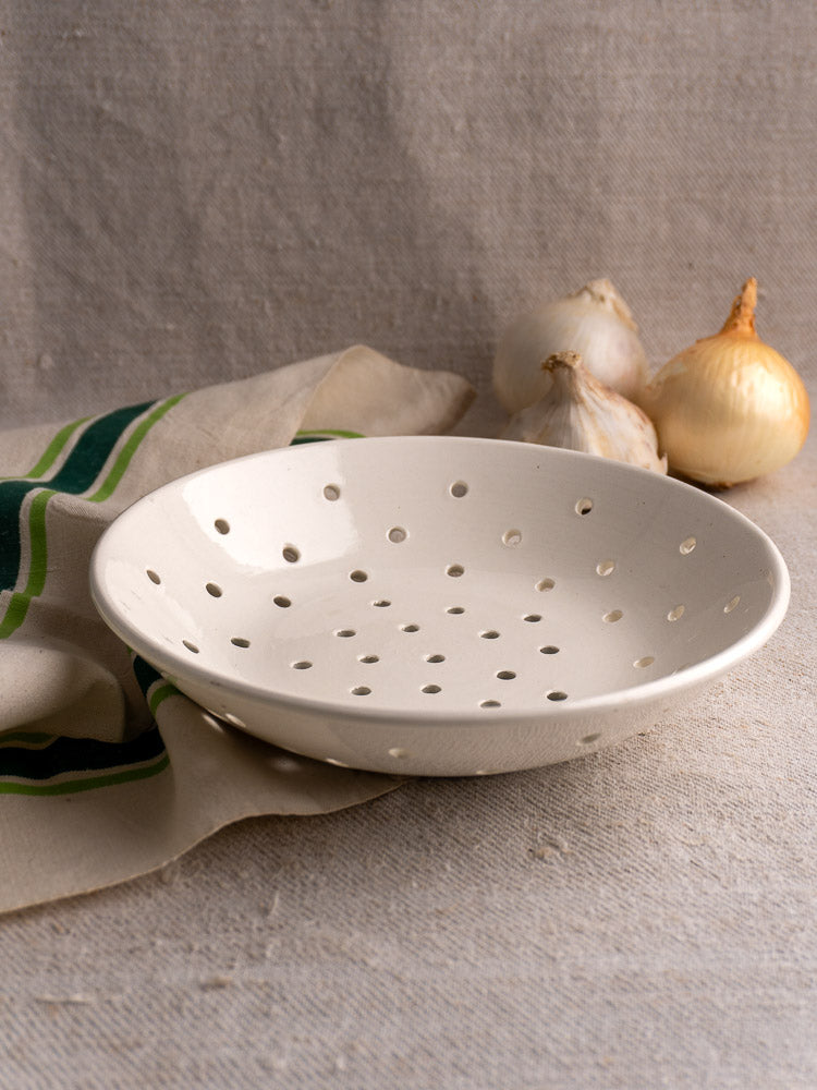 Antique French stoneware berry strainer by Digoin Sarreguemines on beige cloth with garlic and onion.