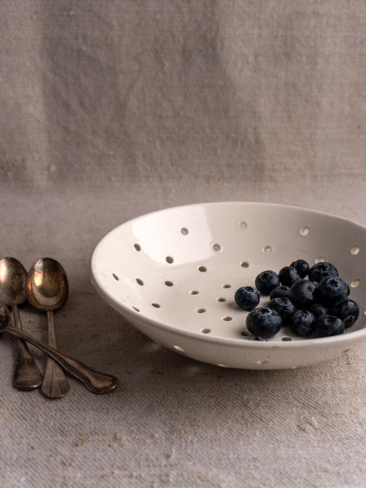 Antique French Digoin Sarreguemines stoneware berry strainer with blueberries, silver spoons on beige textured cloth.