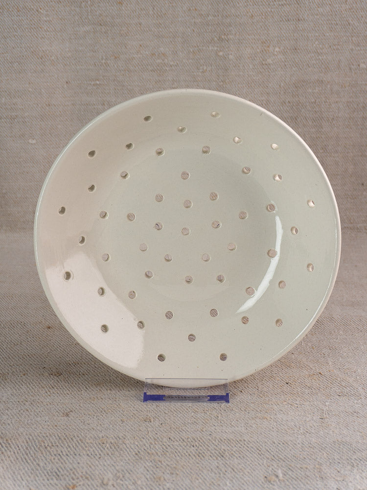 Antique French Digoin Sarreguemines berry strainer, cream stoneware with beige polka dots, on brown fabric background.