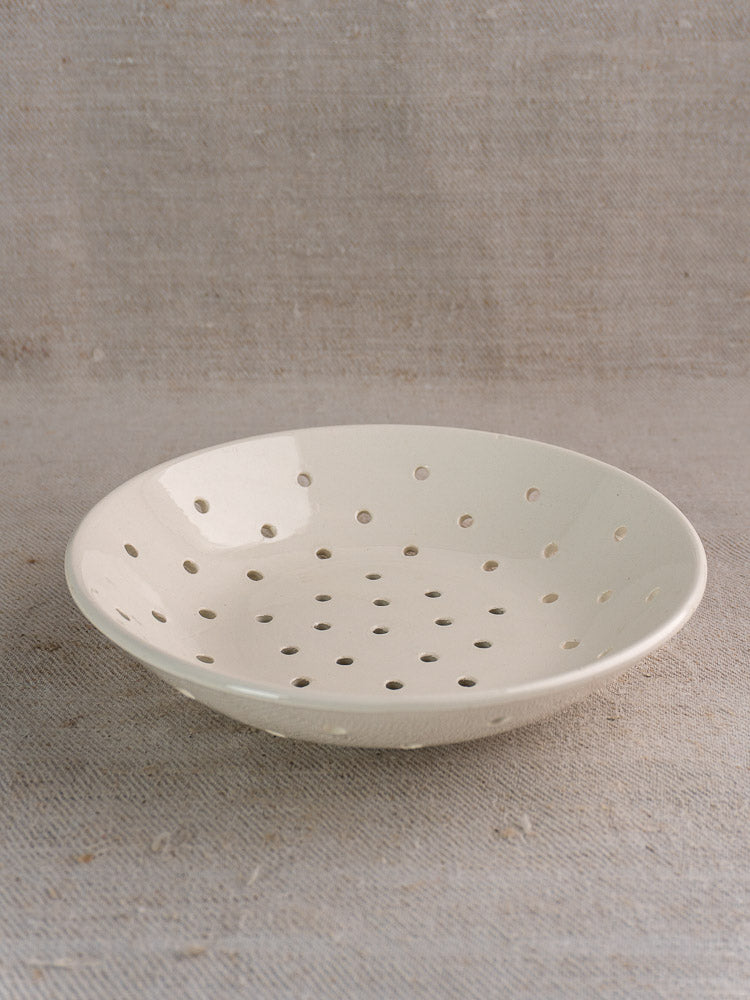 Antique French Digoin Sarreguemines white stoneware berry strainer with perforations on beige linen cloth.