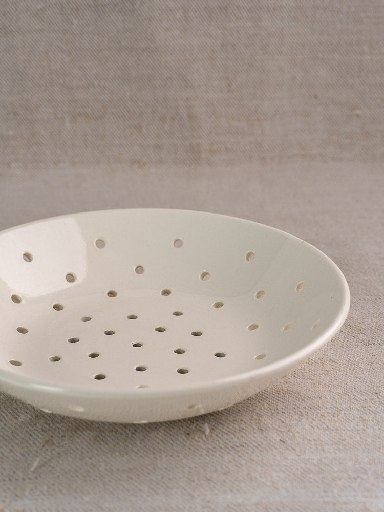 Antique French Digoin Sarreguemines white stoneware berry strainer with drainage holes on beige textured fabric.