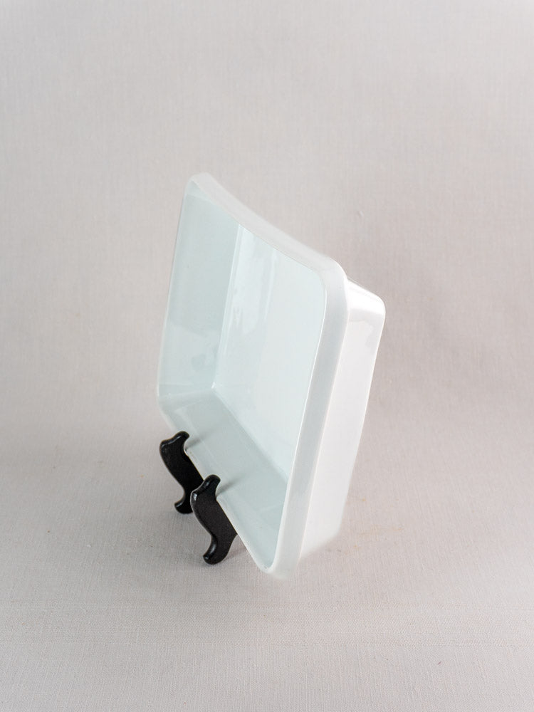 Glossy vintage French porcelain rectangular baking dish displayed on a black stand, neutral light-gray background.