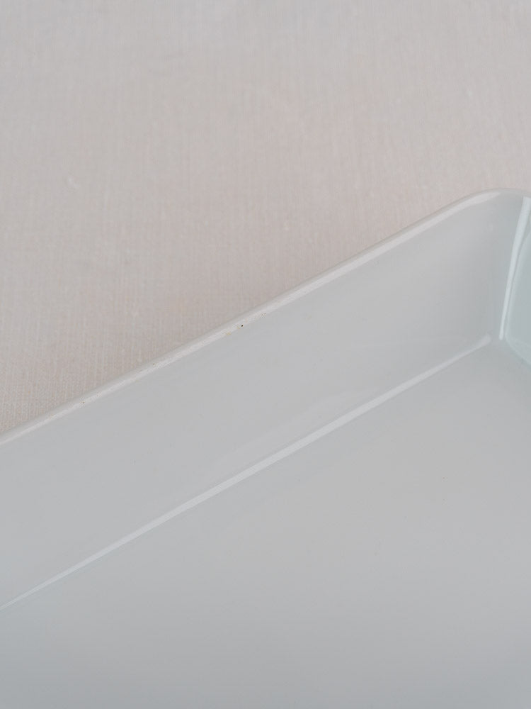 Close-up angled corner of vintage French porcelain baking dish on textured light fabric.